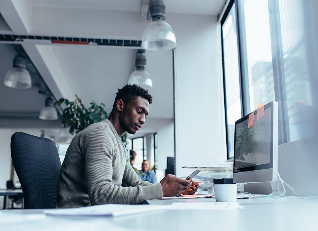 Technology Firm Insurance - Male Executive of a Technology Firm Using His Mobile Phone and Troubleshooting with a Client in the Office