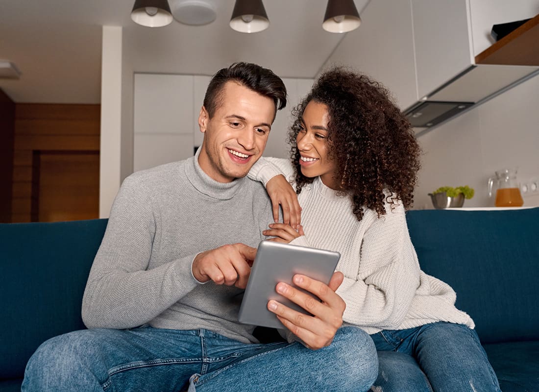 Service Center - Portrait of a Cheerful Young Married Couple Sitting on the Sofa in the Living Room While Using a Tablet